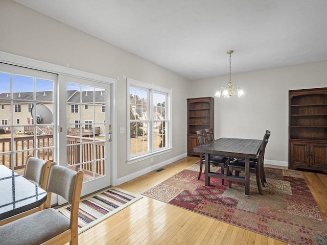 dining room with wood-type flooring, visible vents, a notable chandelier, and baseboards