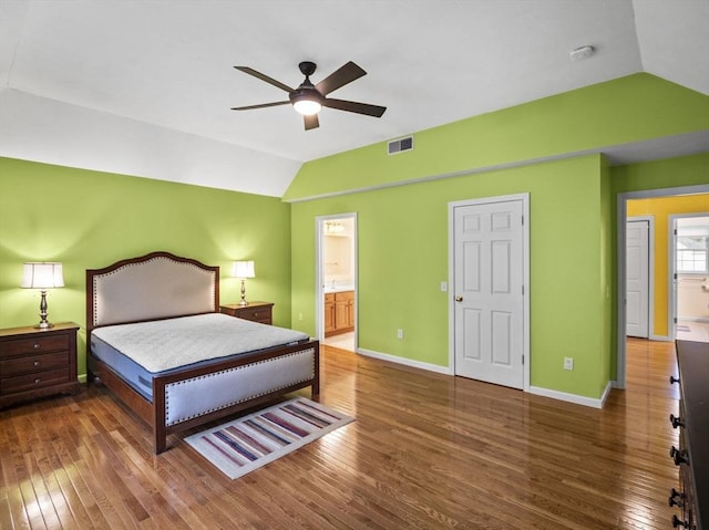 bedroom featuring lofted ceiling, visible vents, baseboards, wood-type flooring, and ensuite bath