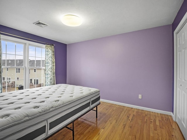 bedroom with a closet, visible vents, baseboards, and hardwood / wood-style flooring