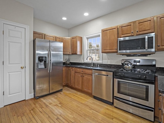 kitchen with light wood-style flooring, appliances with stainless steel finishes, brown cabinets, and a sink