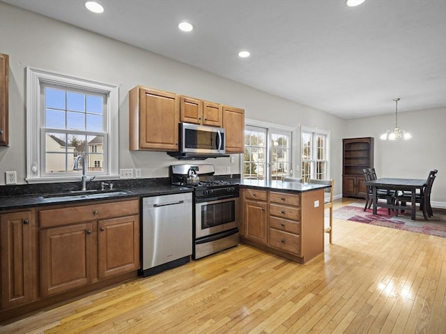 kitchen featuring light wood finished floors, stainless steel appliances, a healthy amount of sunlight, a sink, and a peninsula