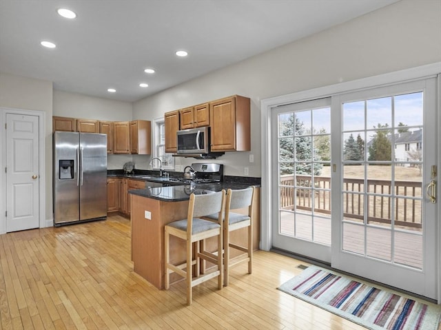 kitchen with stainless steel appliances, a peninsula, a sink, light wood finished floors, and brown cabinetry