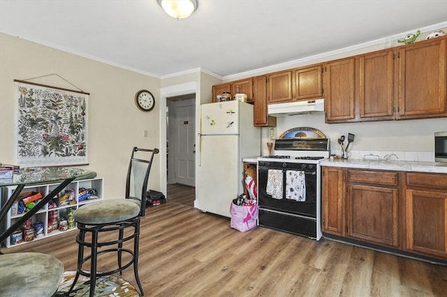 kitchen featuring freestanding refrigerator, gas range, under cabinet range hood, light countertops, and brown cabinets