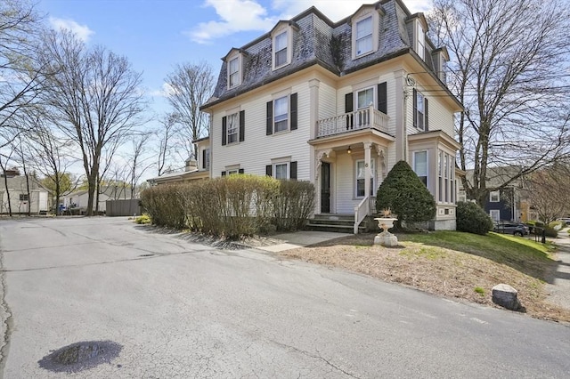 second empire-style home featuring a balcony and mansard roof