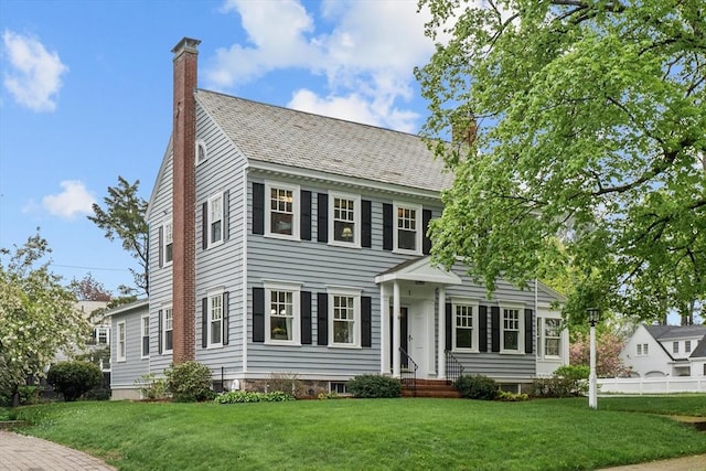 colonial inspired home with a chimney, a front lawn, and a high end roof
