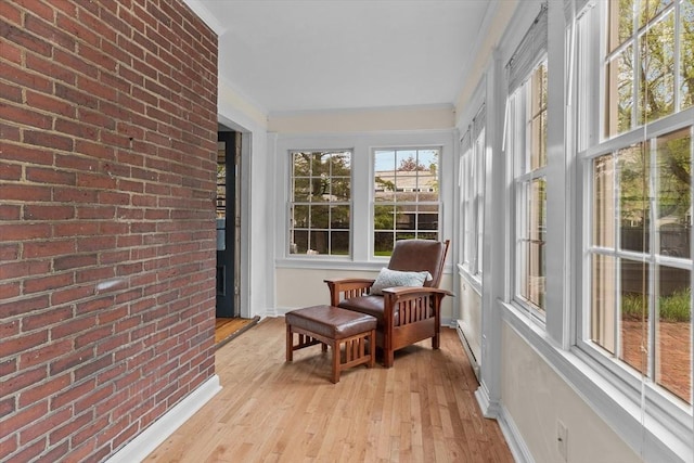 sunroom / solarium featuring hardwood / wood-style floors, brick wall, crown molding, baseboards, and baseboard heating