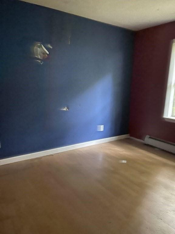 spare room featuring a baseboard radiator, wood finished floors, and baseboards