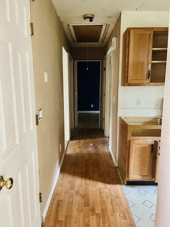 hall with light wood finished floors, attic access, and baseboards