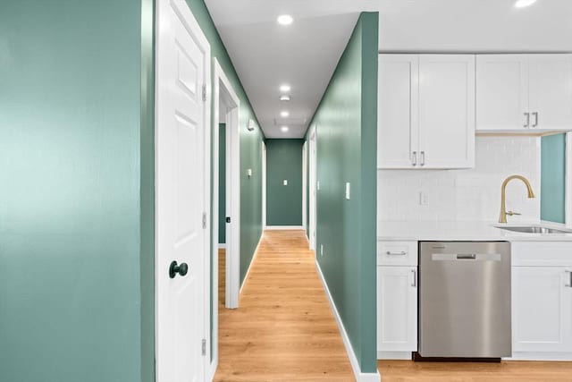 kitchen with stainless steel dishwasher, light wood-style floors, white cabinetry, and a sink