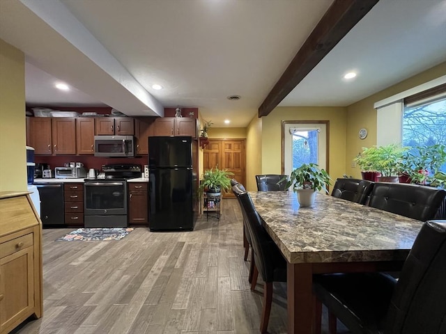 kitchen with a kitchen bar, black appliances, dark stone countertops, beamed ceiling, and light hardwood / wood-style floors