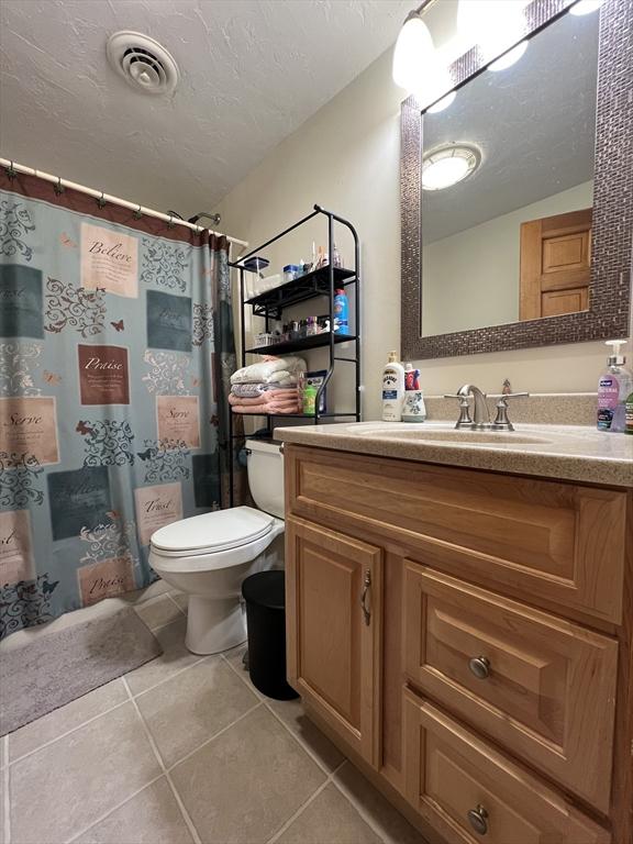 bathroom featuring vanity, tile patterned flooring, toilet, a textured ceiling, and curtained shower