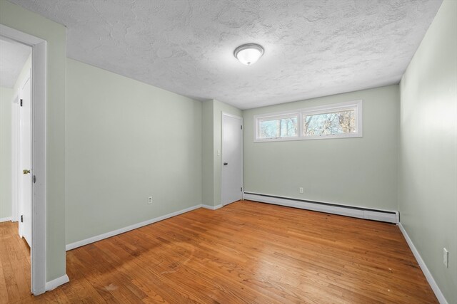 empty room with a textured ceiling, baseboard heating, and light hardwood / wood-style flooring