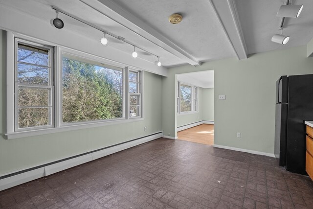 interior space with beam ceiling, black refrigerator, a healthy amount of sunlight, and a baseboard heating unit