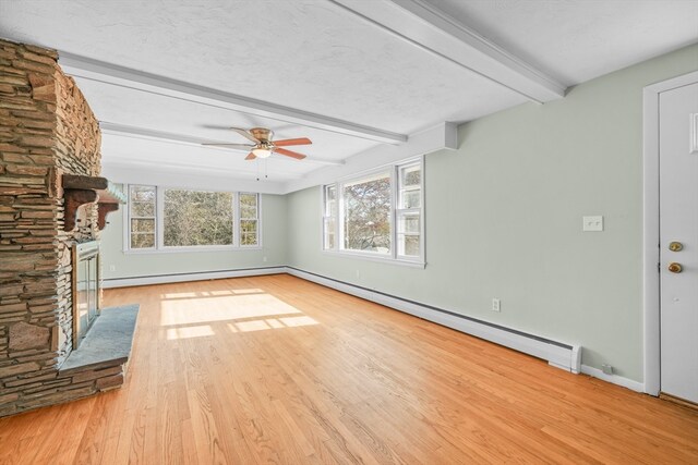 unfurnished living room featuring beamed ceiling, light hardwood / wood-style flooring, a stone fireplace, and a baseboard heating unit