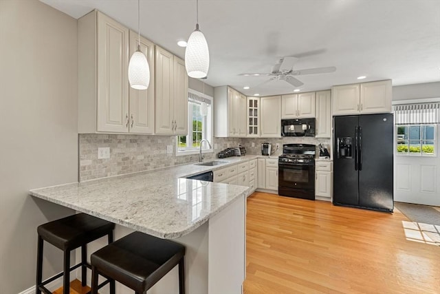 63 Prospect St Unit 2, Woburn, MA 01801 - kitchen featuring black appliances, a sink, a peninsula, light wood-style floors, and decorative light fixtures