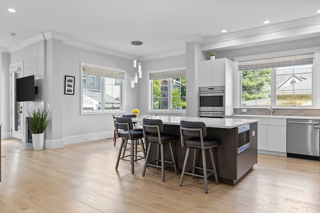 kitchen with a kitchen island, hanging light fixtures, crown molding, white cabinetry, and appliances with stainless steel finishes