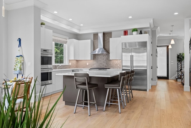 kitchen featuring appliances with stainless steel finishes, wall chimney exhaust hood, white cabinetry, and a kitchen island