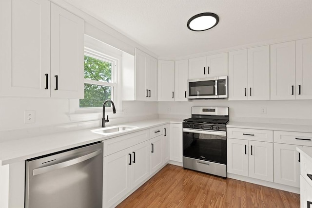126 Willard St Unit D, Lowell, MA 01850 - kitchen with appliances with stainless steel finishes, a sink, white cabinetry, light countertops, and light wood-style flooring
