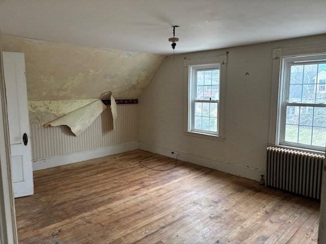 additional living space with a healthy amount of sunlight, wood-type flooring, radiator, and vaulted ceiling