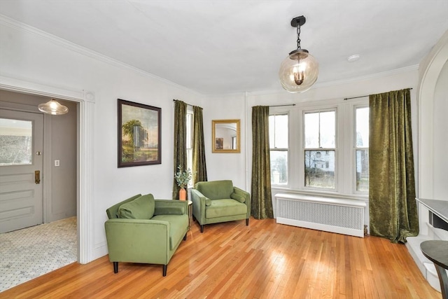 sitting room with radiator heating unit, light wood-type flooring, and ornamental molding