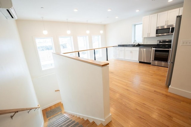 kitchen with a wall mounted AC, hanging light fixtures, light wood-type flooring, appliances with stainless steel finishes, and white cabinets