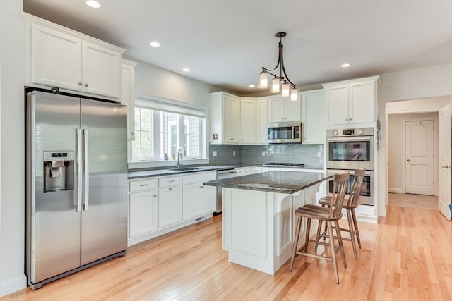 kitchen with light hardwood / wood-style flooring, appliances with stainless steel finishes, white cabinetry, sink, and a kitchen island