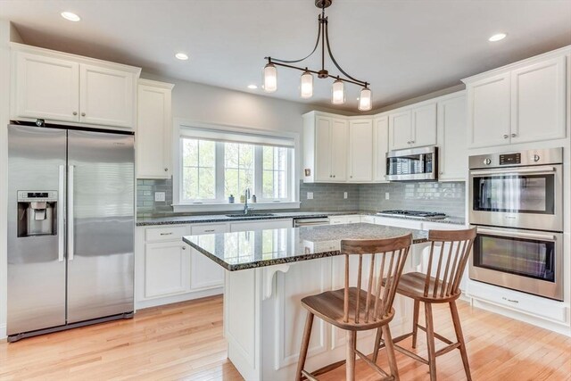 kitchen with a kitchen island, light wood-type flooring, appliances with stainless steel finishes, and dark stone counters