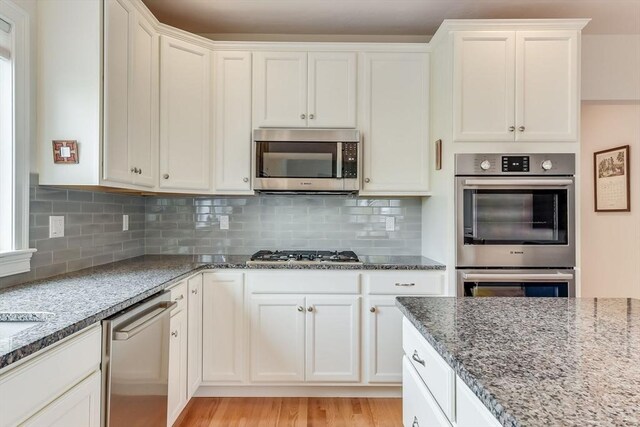 kitchen featuring stainless steel appliances, light wood-type flooring, white cabinetry, and decorative backsplash