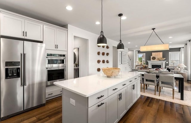 kitchen featuring a fireplace, a kitchen island, stainless steel appliances, and dark wood finished floors