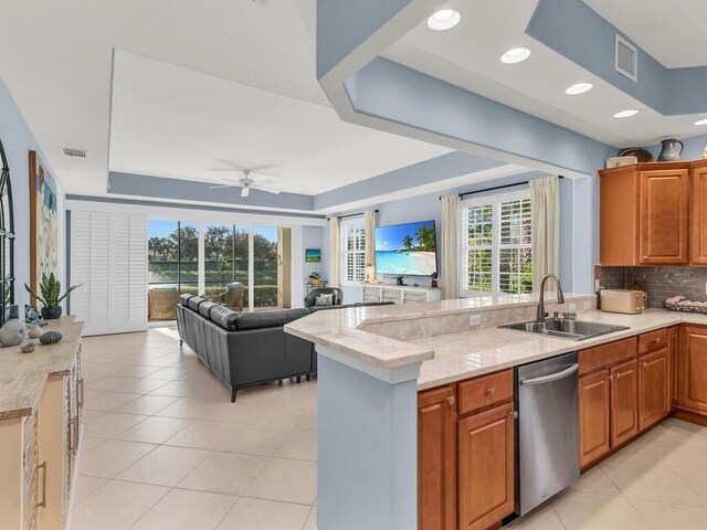 kitchen with light stone countertops, kitchen peninsula, a raised ceiling, ceiling fan, and sink