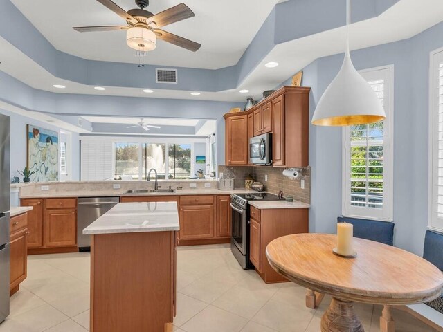 kitchen with a wealth of natural light, stainless steel appliances, sink, decorative light fixtures, and a center island