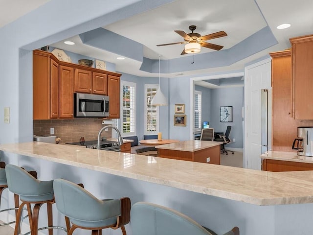 kitchen with decorative backsplash, a kitchen bar, kitchen peninsula, and a tray ceiling