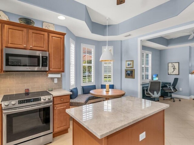 kitchen with a center island, decorative backsplash, appliances with stainless steel finishes, a tray ceiling, and decorative light fixtures