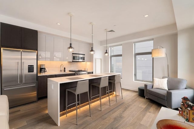 kitchen featuring appliances with stainless steel finishes, pendant lighting, light hardwood / wood-style flooring, a breakfast bar, and a center island