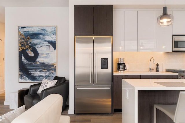 kitchen featuring white cabinetry, hardwood / wood-style flooring, hanging light fixtures, and appliances with stainless steel finishes