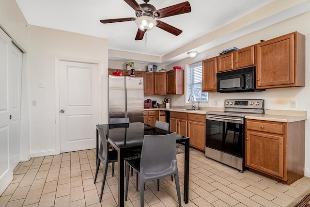 kitchen featuring light countertops, appliances with stainless steel finishes, brown cabinetry, a ceiling fan, and a sink