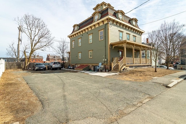 view of front facade featuring mansard roof, aphalt driveway, a porch, and fence