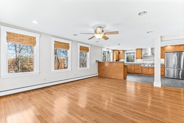 unfurnished living room featuring ceiling fan, light hardwood / wood-style flooring, and a baseboard heating unit