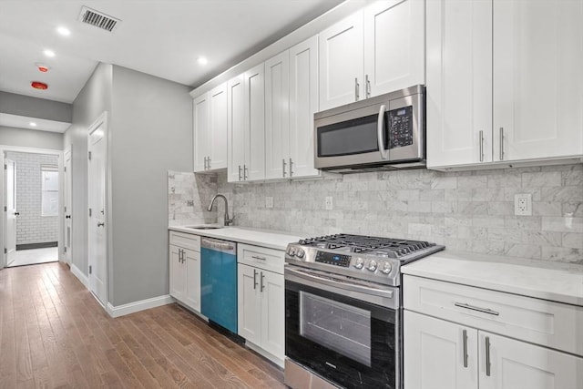 kitchen featuring appliances with stainless steel finishes, a sink, light countertops, wood finished floors, and recessed lighting