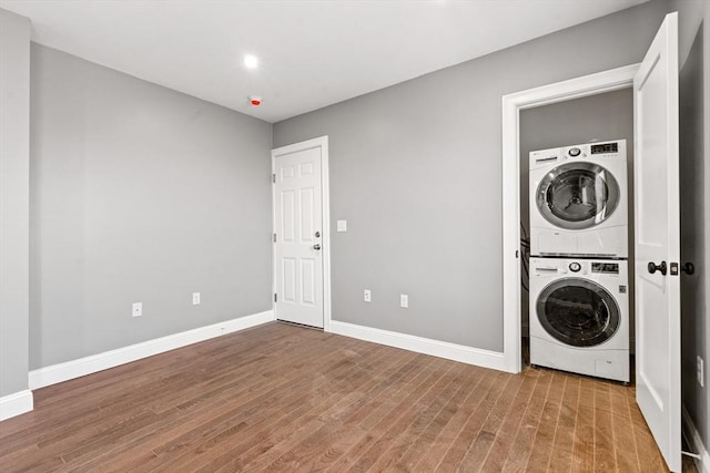 laundry area featuring stacked washer / dryer, wood finished floors, and baseboards