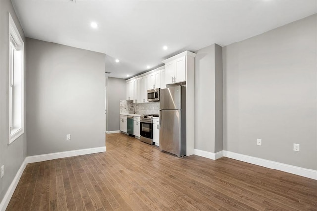 unfurnished living room with wood finished floors, baseboards, a sink, and recessed lighting