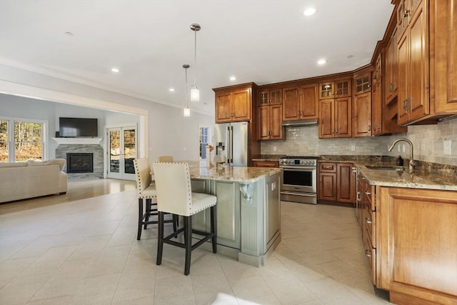 kitchen with a center island with sink, sink, hanging light fixtures, light stone counters, and stainless steel appliances