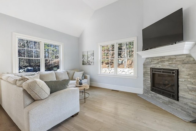 living room with a stone fireplace, vaulted ceiling, and light wood-type flooring