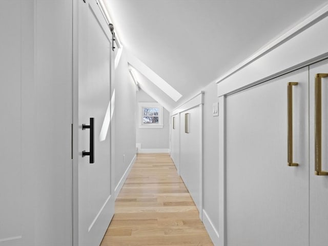 hallway featuring lofted ceiling with skylight and light hardwood / wood-style floors