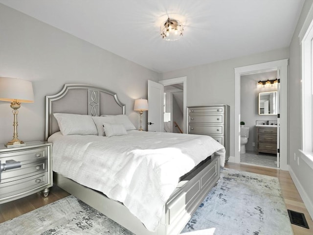 bedroom with dark wood-type flooring and connected bathroom