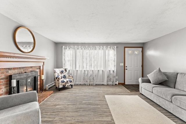 living area with a textured ceiling, a baseboard radiator, wood finished floors, baseboards, and a brick fireplace