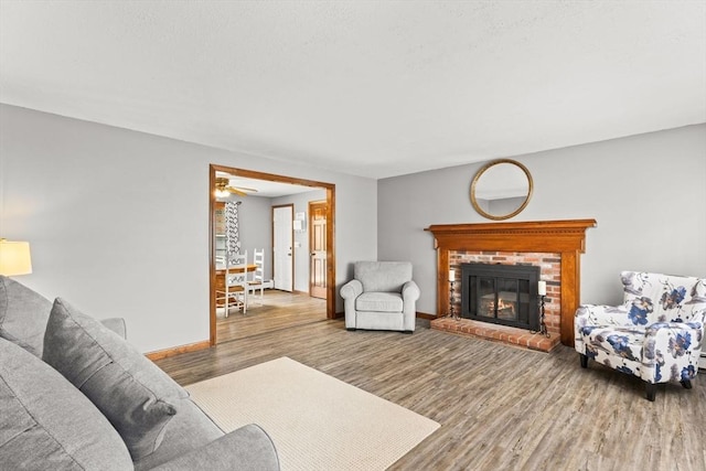 living room with a brick fireplace, baseboards, and wood finished floors