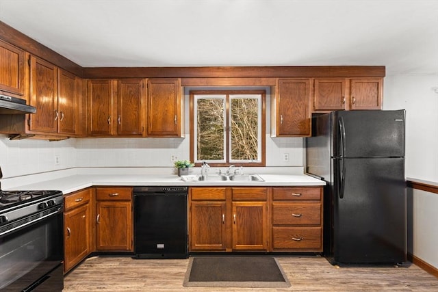 kitchen featuring black appliances, light wood finished floors, a sink, and light countertops