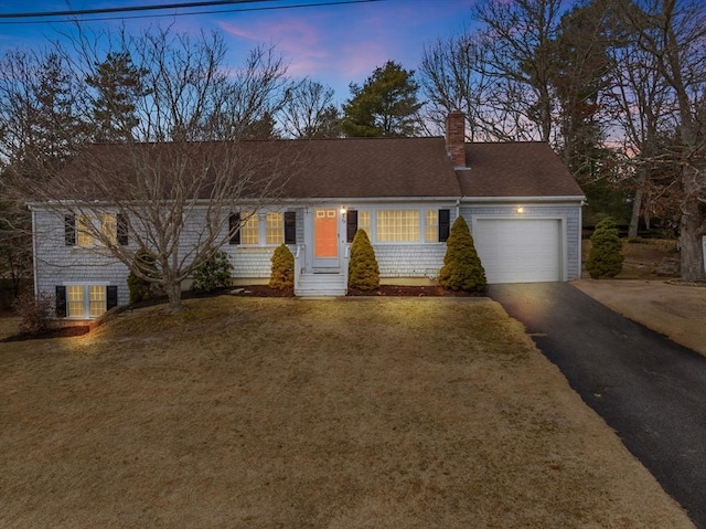 ranch-style house with aphalt driveway, a garage, a shingled roof, a lawn, and a chimney