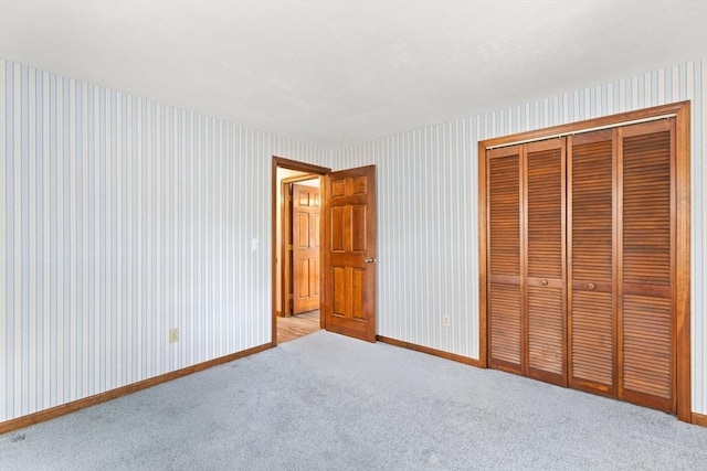 unfurnished bedroom featuring baseboards, a closet, light colored carpet, and wallpapered walls